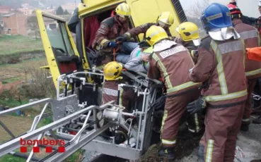Fotografia de rescat amb llitera: diversos bombers extreuen una persona ferida de la cabina d'un camió groc accidentat, recolzant-se en la cistella metàl·lica d'una autoescala adaptada per a la llitera.