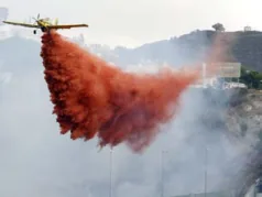 Avió groc en vol baix que deixa anar una gran descàrrega de retardant vermell sobre una zona amb fum.